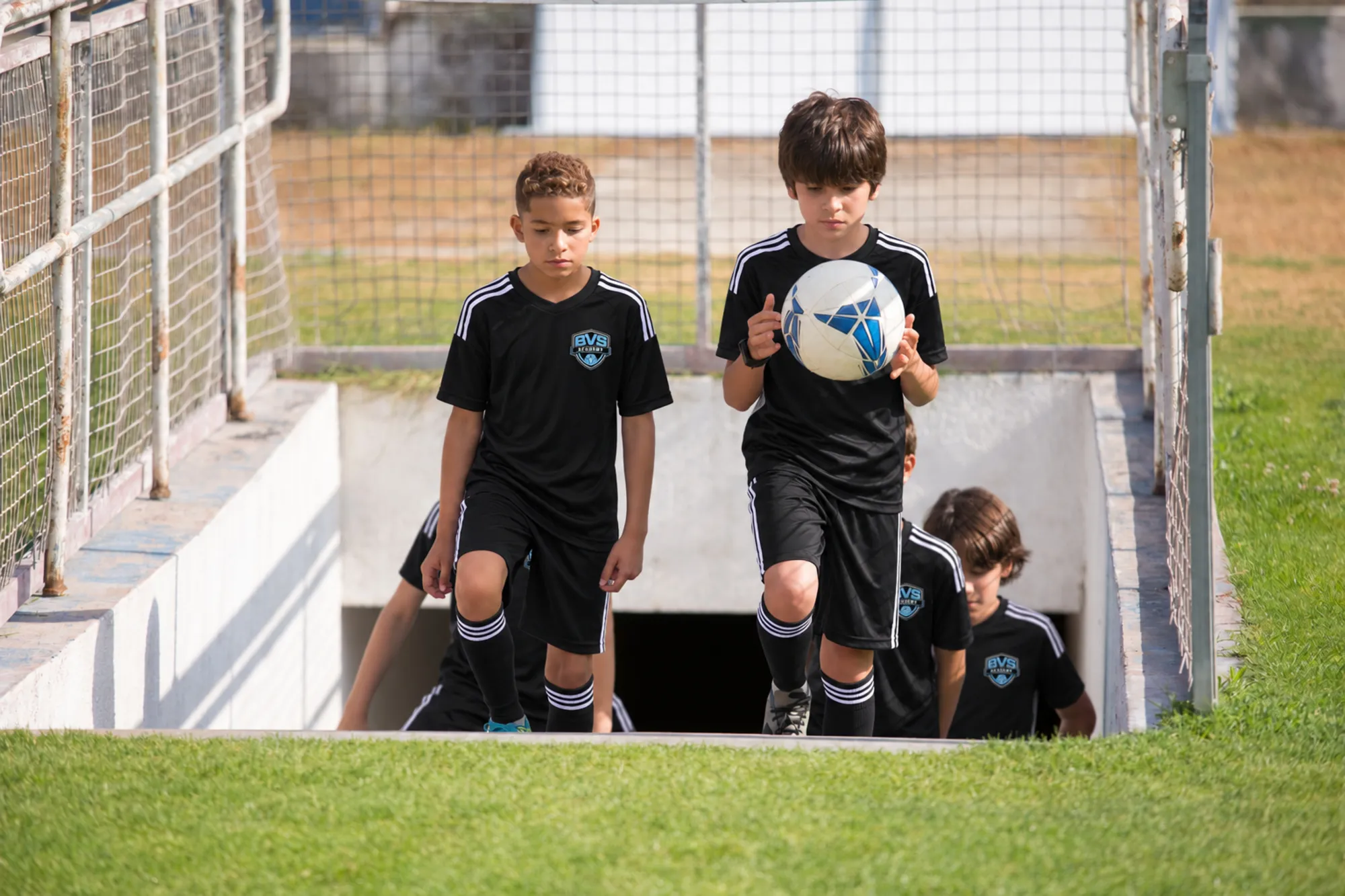 Young players walking out of the tunnel onto a stadium field